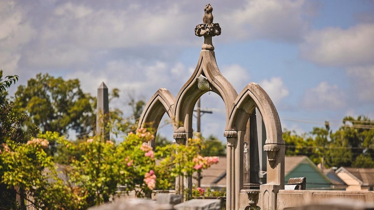 Gothic-style stone monument at Greenwood Cemetery with trees and a partly cloudy sky behind it