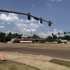 Traffic signals at a wide intersection under a partly cloudy sky