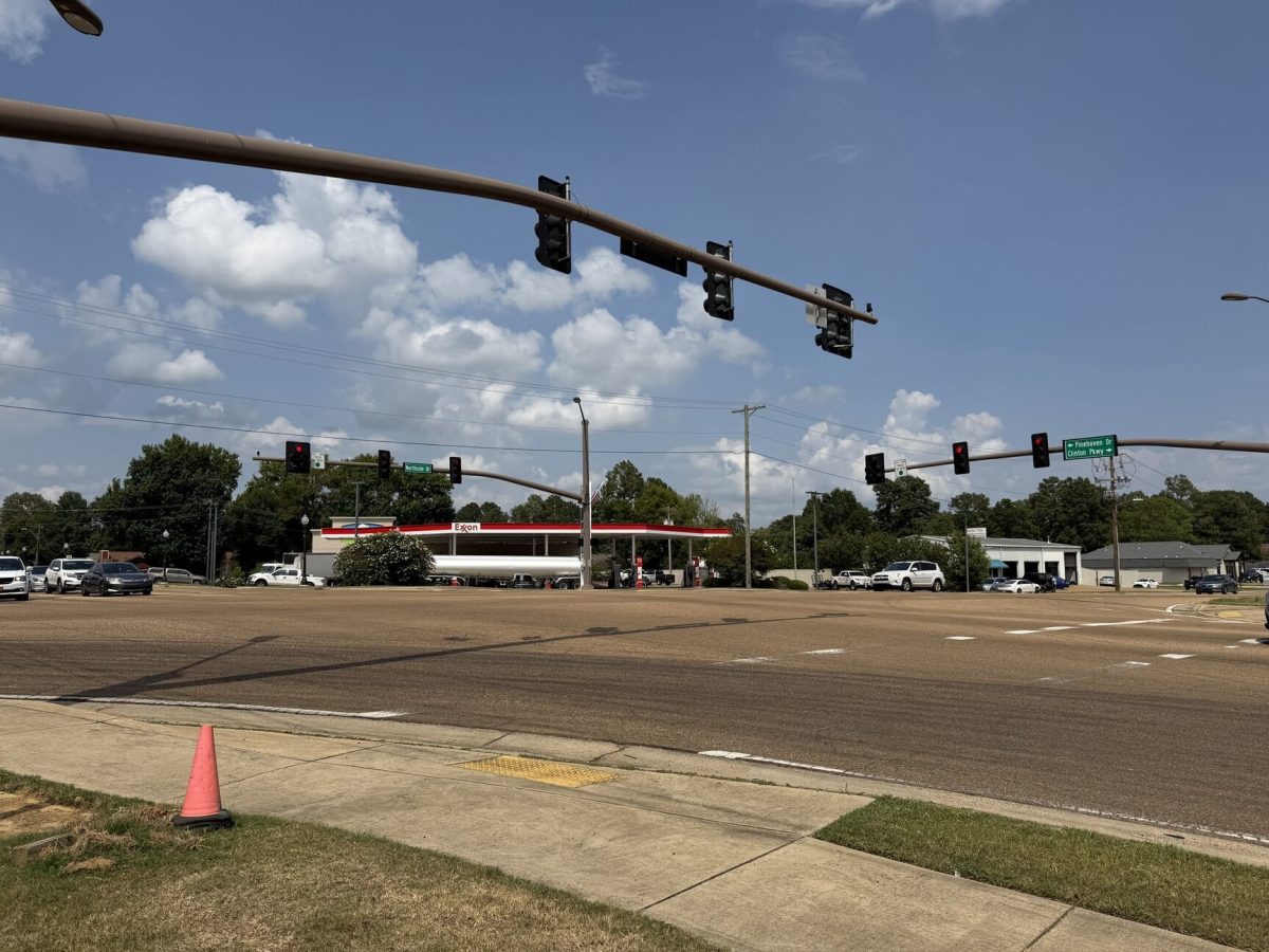 Traffic signals at a wide intersection under a partly cloudy sky