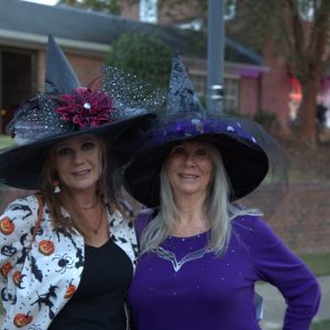 Two women in decorated witch hats posing outdoors