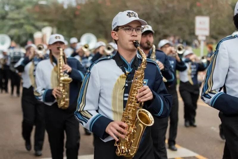 MC marching band members playing saxophones in a parade