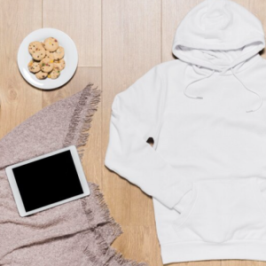white hoodie on a wood backdrop with cookies, hot chocolate and an ipad on a blanket