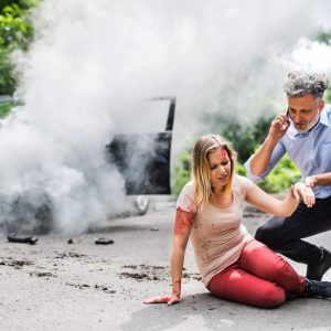 Young woman by the car after an accident and a man making a phone call