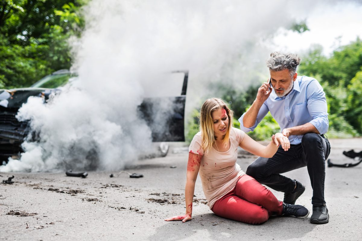 Young woman by the car after an accident and a man making a phone call