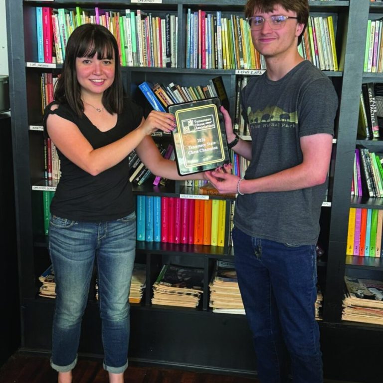 James Dove receiving the first place plaque from the chief tournament director in front of a bookshelf