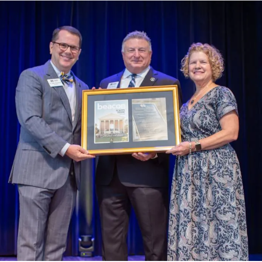 MC President Blake Thompson presents a framed copy of the most recent issue of 'The Beacon,' MC's official alumni and news magazine, to Jim Turcotte, MC vice president and special assistant to the president, in recognition of Turcotte's 32 years of service to the institution. Turcotte's wife, Jenny, is at right.
