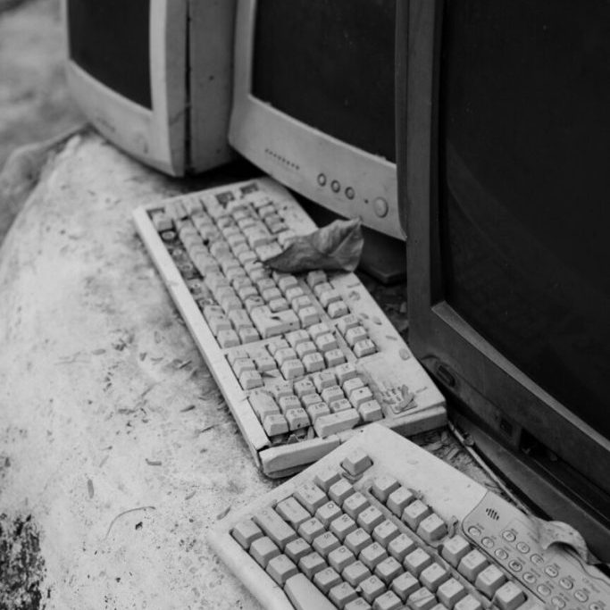 Old computer monitors and keyboards piled together, shown in black and white