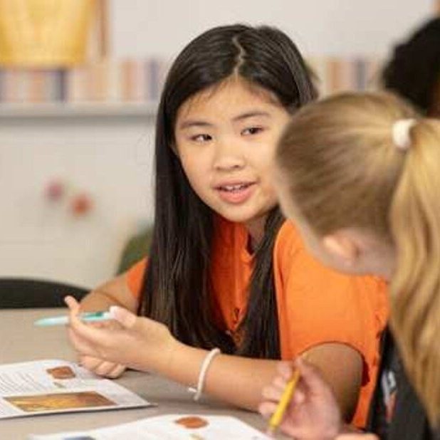 Elementary students at a classroom table working on a project with pencils and papers