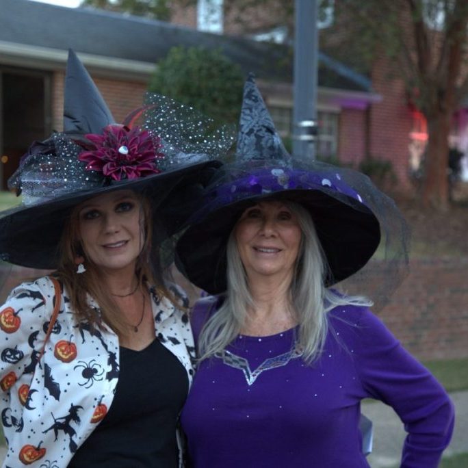 Two women in decorated witch hats posing outdoors